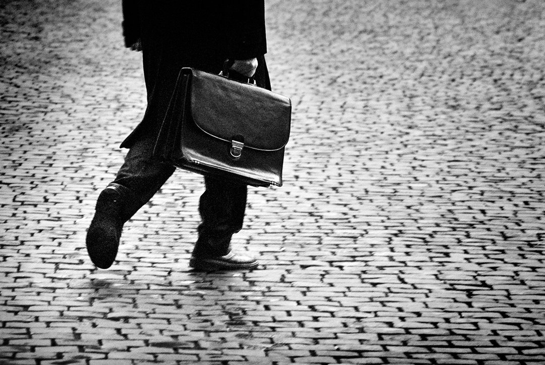 A person carrying a briefcase crosses a cobbled surface.